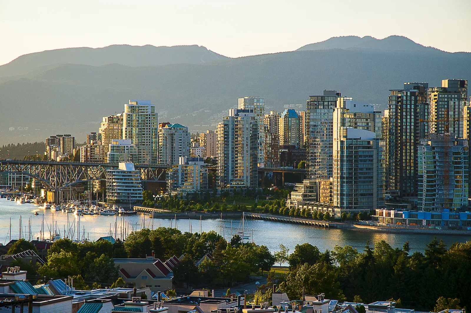 High-rise city skyline situated along a waterfront with a bridge and mountain backdrop.