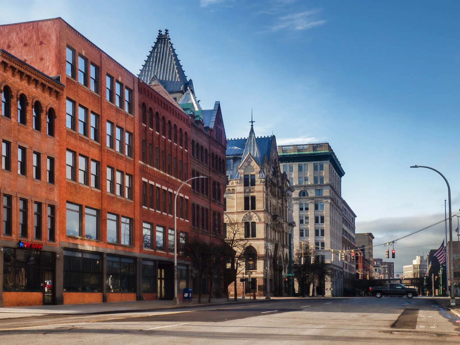 An empty downtown street lined with historic red brick and stone buildings featuring distinct rooflines under a bright blue sky.
