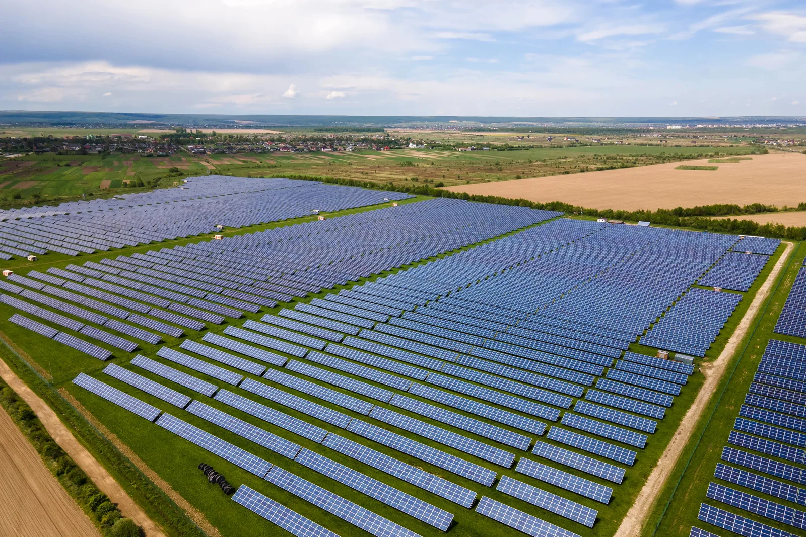 Aerial view of a utility-scale solar farm featuring rows of blue panels across a green field.