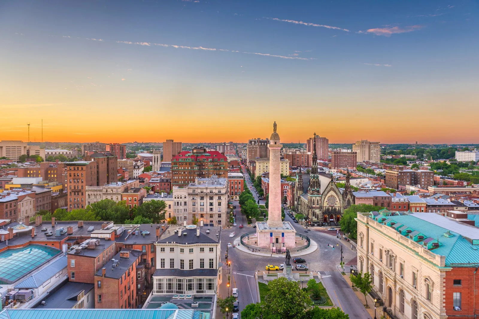 Aerial view of a historic city square and monument under a sunset sky.