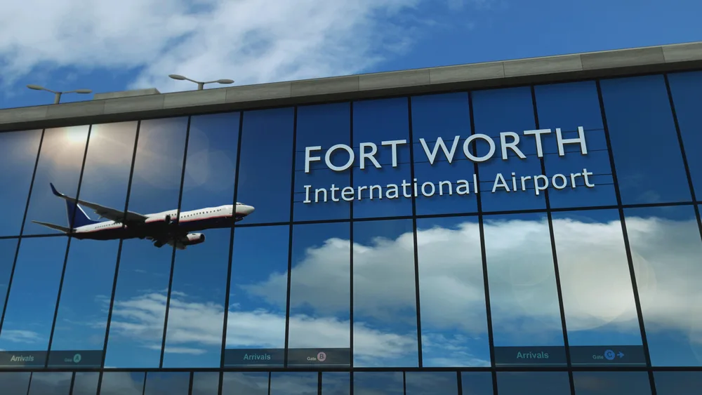 Glass terminal facade reflecting an airplane and Fort Worth International Airport signage.
