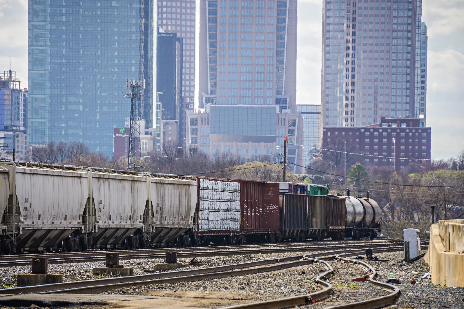 A freight train on railway tracks in front of a modern city skyline.