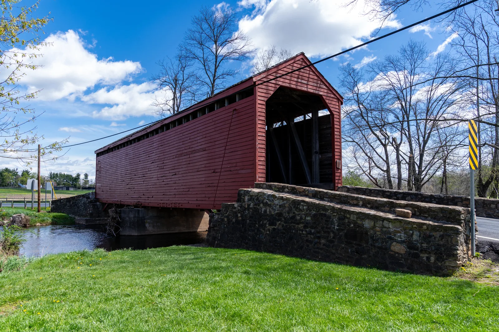 A historic red covered bridge spanning a small creek under a blue sky.