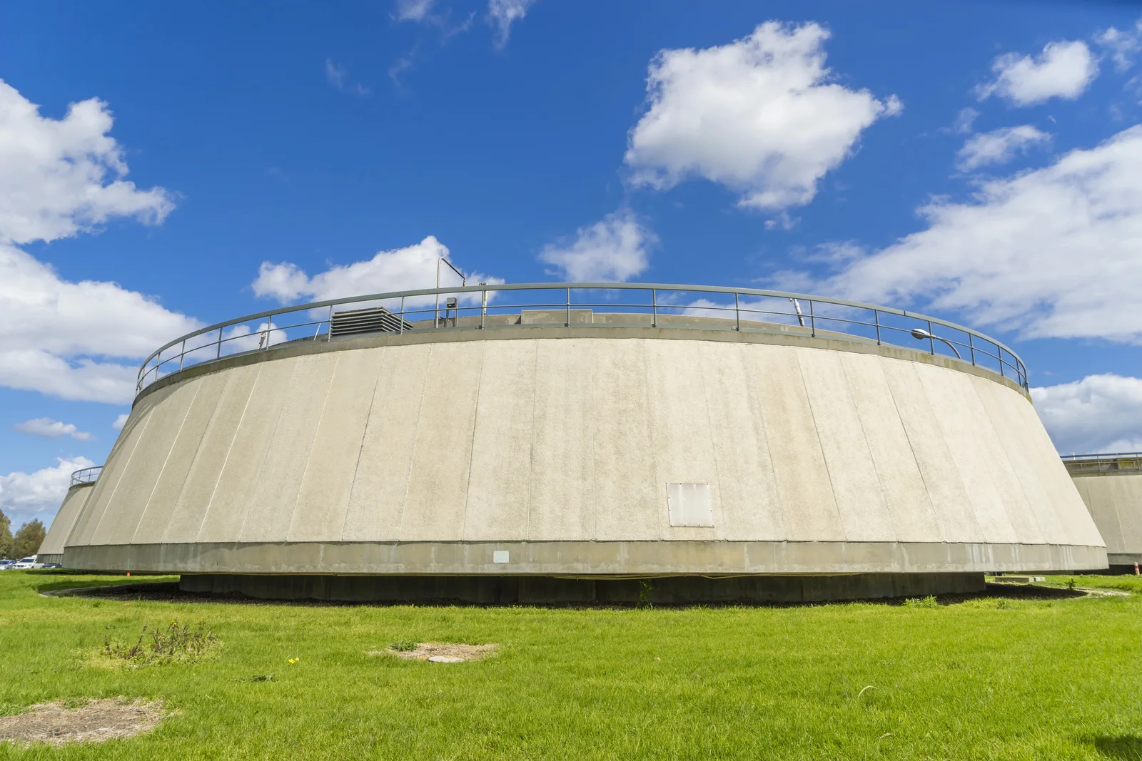 A circular concrete water treatment tank on a grassy field.