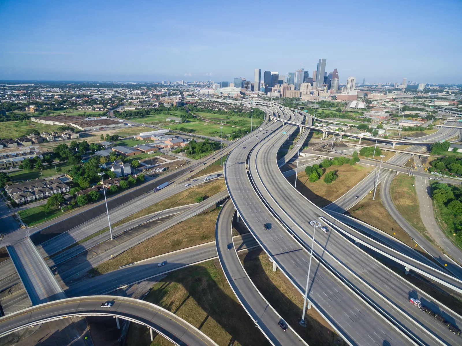 Aerial view of multi-lane highway interchange with downtown skyline in the background. Cars and trucks are on the roads.