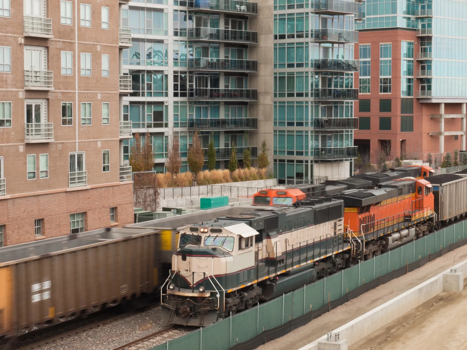 A freight train moves along a track passing in front of modern urban high-rise buildings.