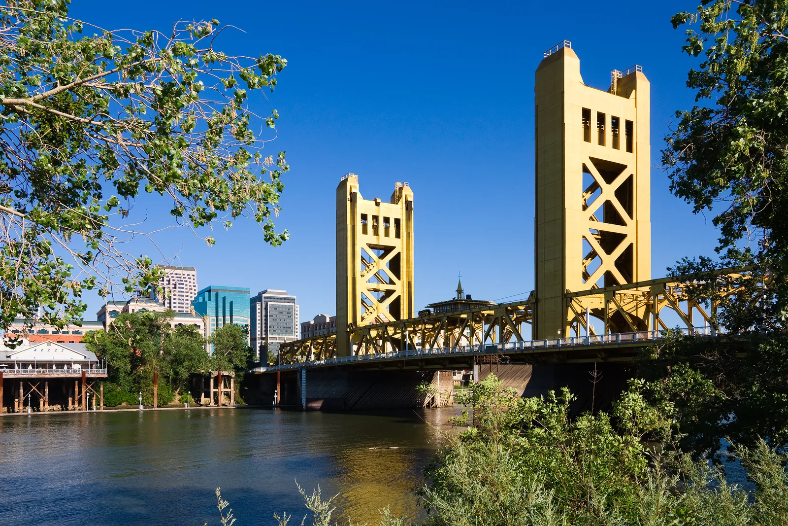 Yellow vertical-lift bridge spanning a river against a city skyline.