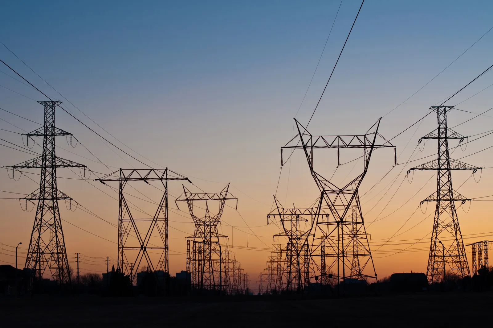 High-voltage power transmission towers silhouetted against a dusk sky.