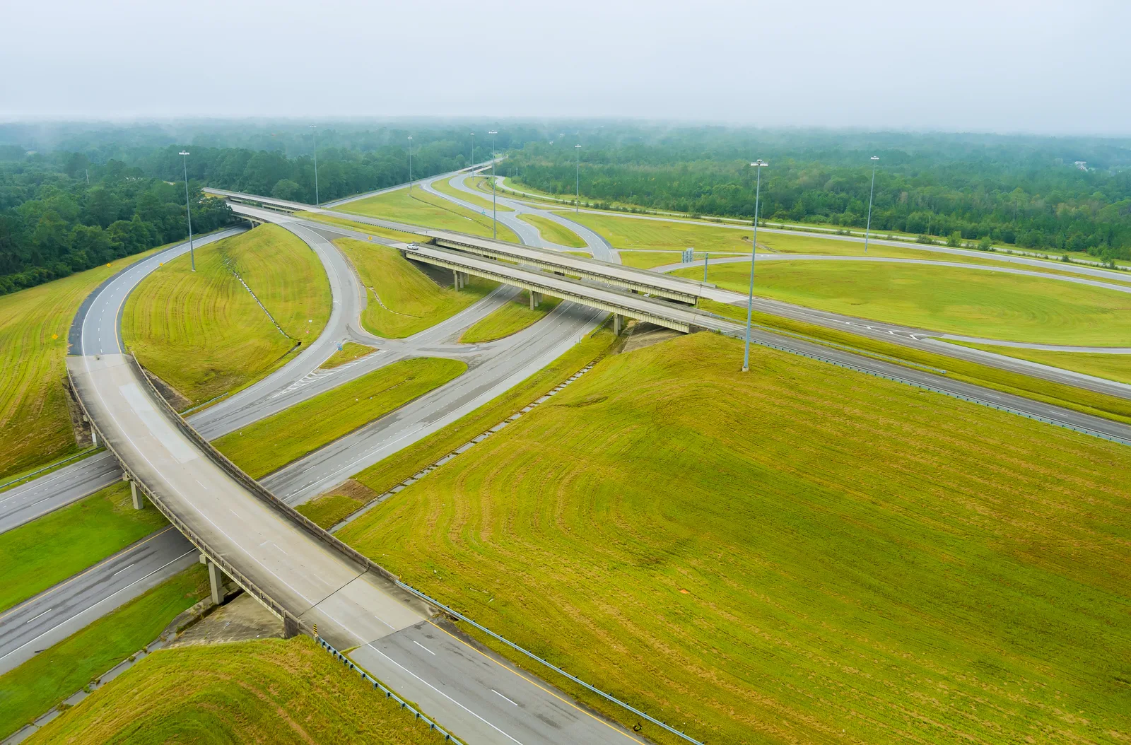 Multi-level concrete highway interchange surrounded by green fields.