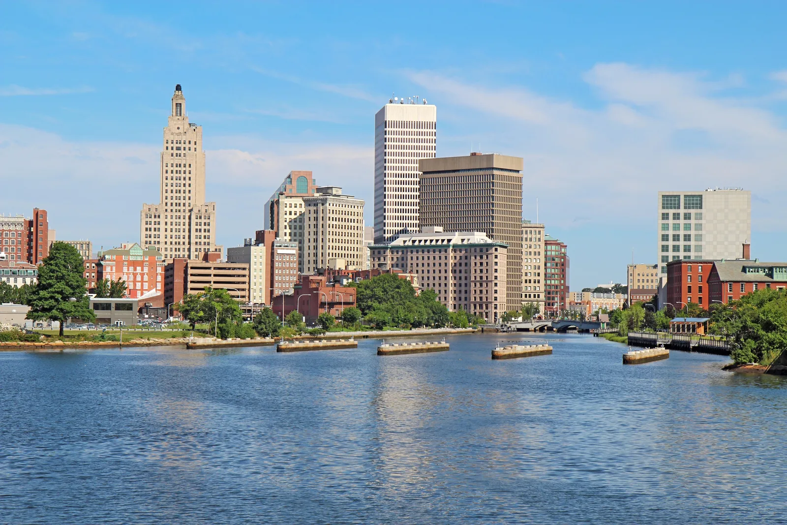 City skyline along a riverfront featuring high-rise buildings under a blue sky.